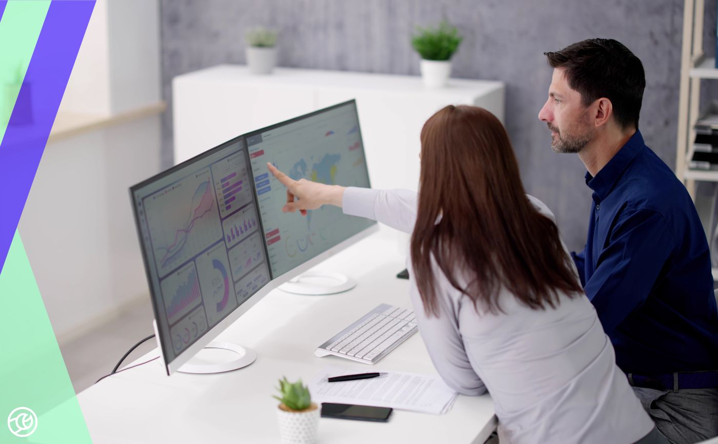 Two colleagues reviewing a marketing analytics dashboard on a large computer monitor in a professional office setting.