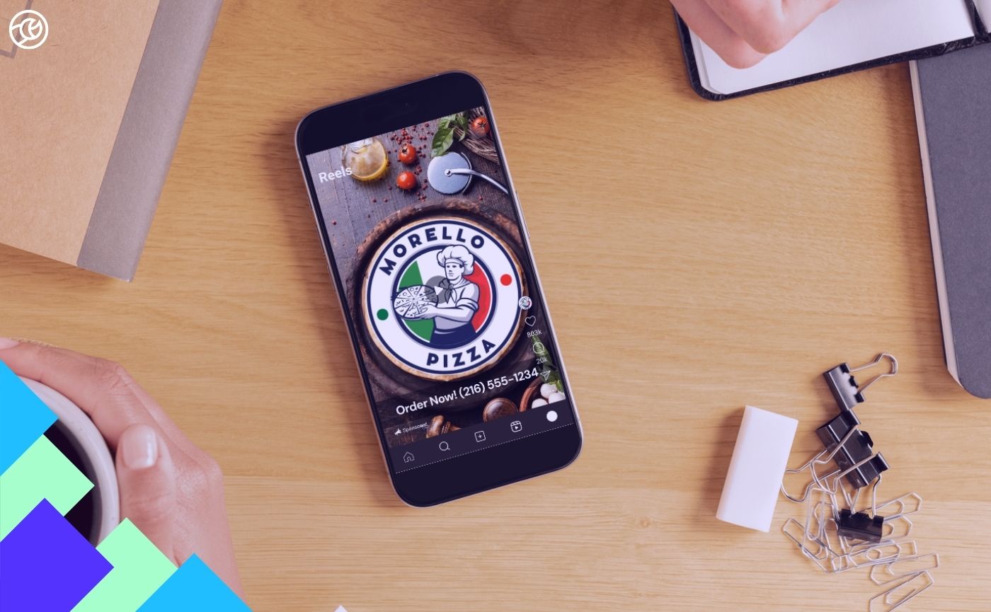 A smartphone on a wooden desk displaying a video of Morello Pizza on Instagram Reels, surrounded by office supplies.