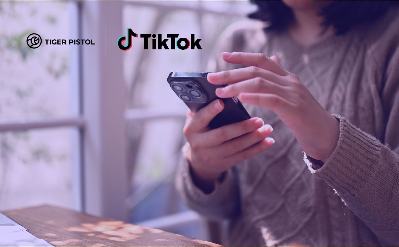 A person holding a smartphone showing the TikTok logo alongside the Tiger Pistol logo in an overlay graphic.